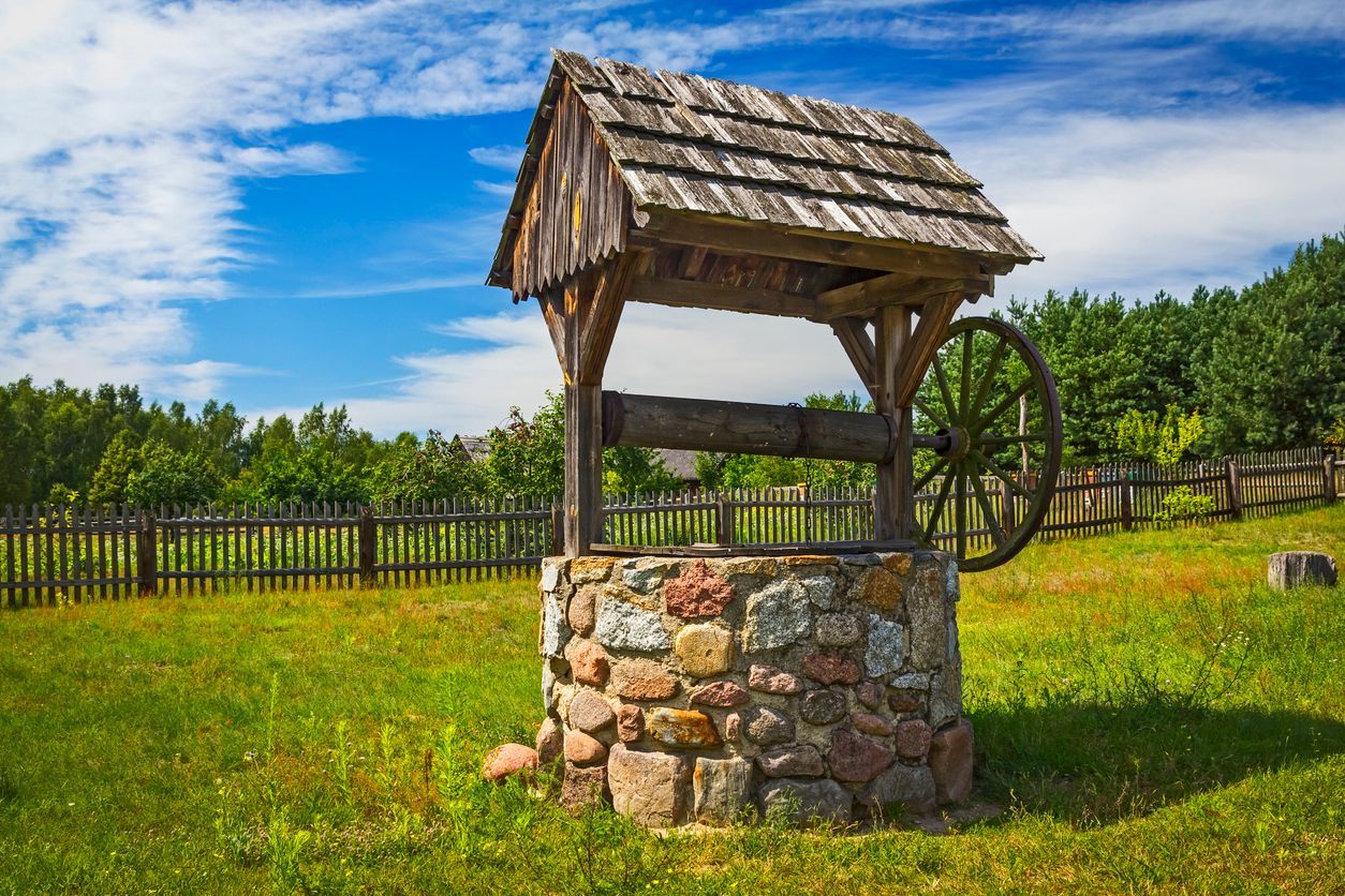An old, rustic stone well with a wood shingle roof is in the backyard of the house