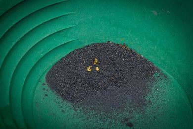 A green pan filled with black sand and gold nuggets.