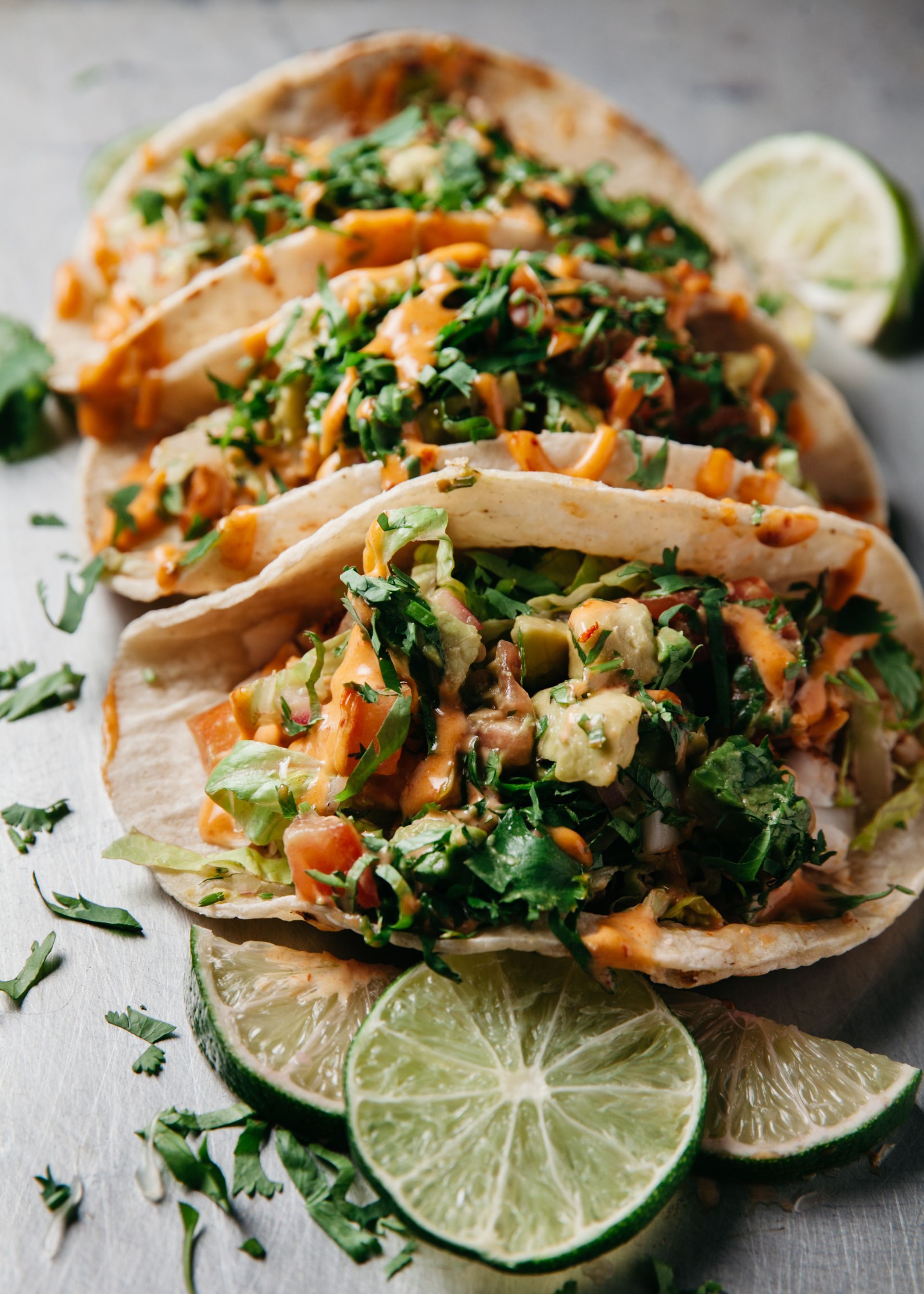 A close up of a stack of tacos with lime wedges on a table.