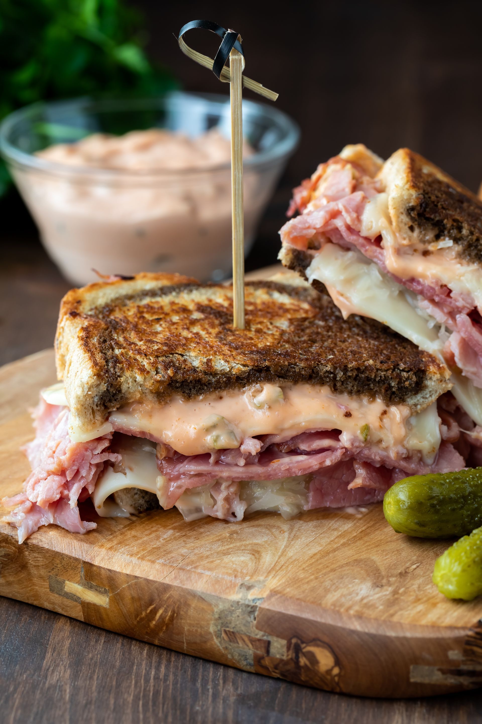 A grilled corned beef sandwich with pickles on a cutting board.