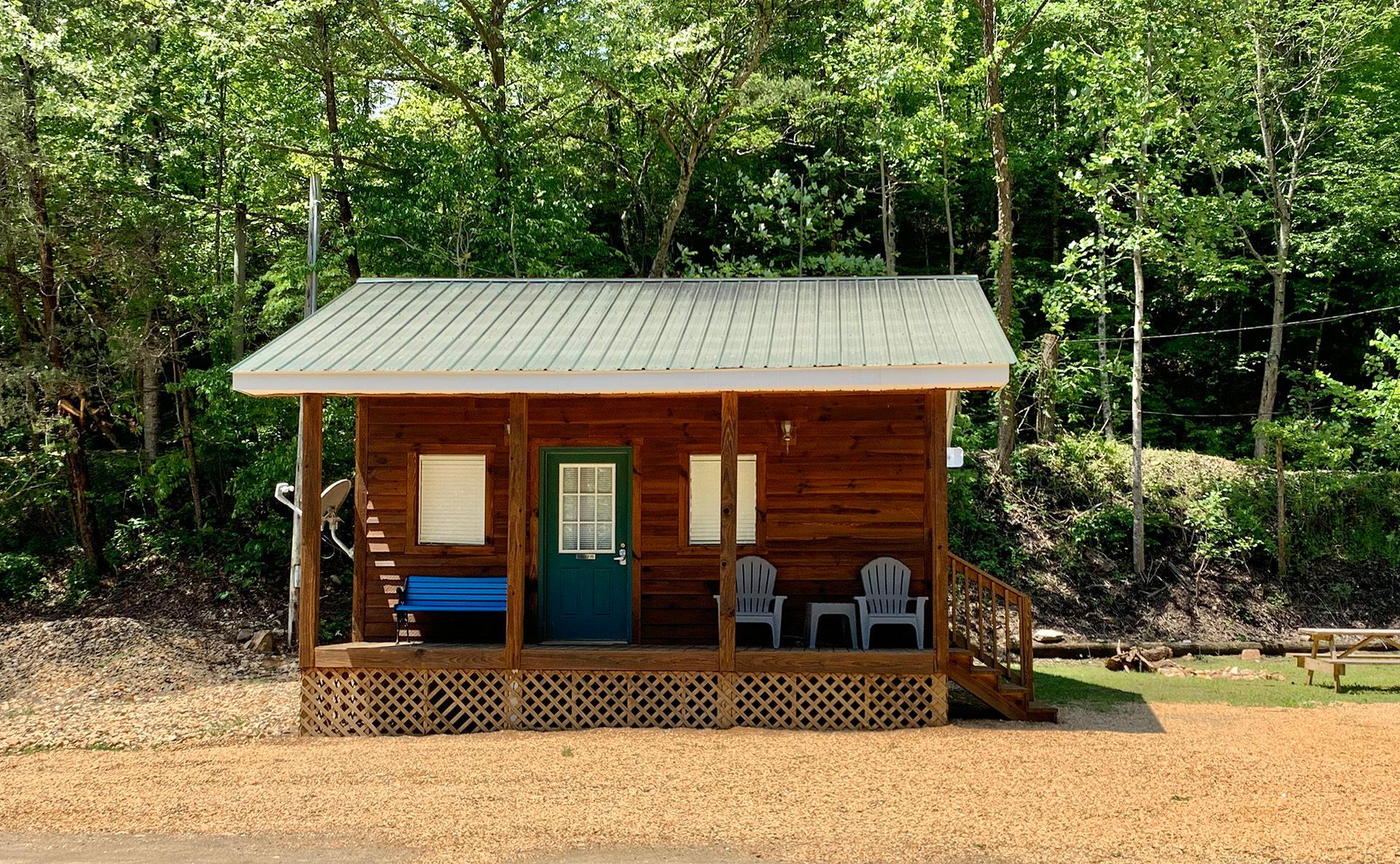 A small log cabin with a porch and chairs in the woods.