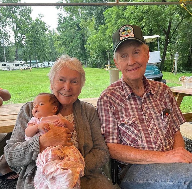 A man and a woman are sitting at a picnic table holding a baby.