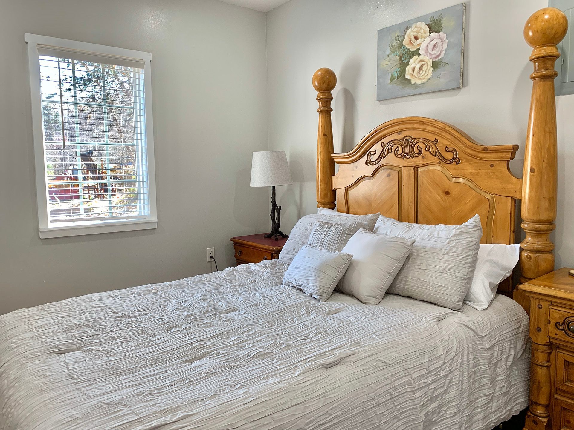 A bedroom with a bed , nightstand , lamp and window.