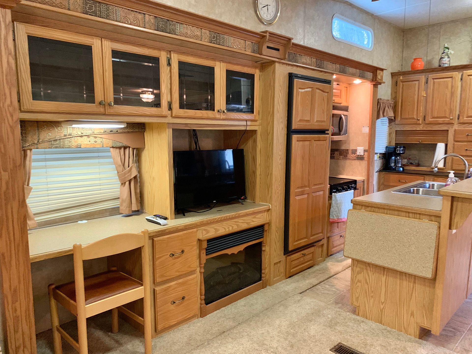 A kitchen with wooden cabinets , a desk , a television , a refrigerator and a sink.