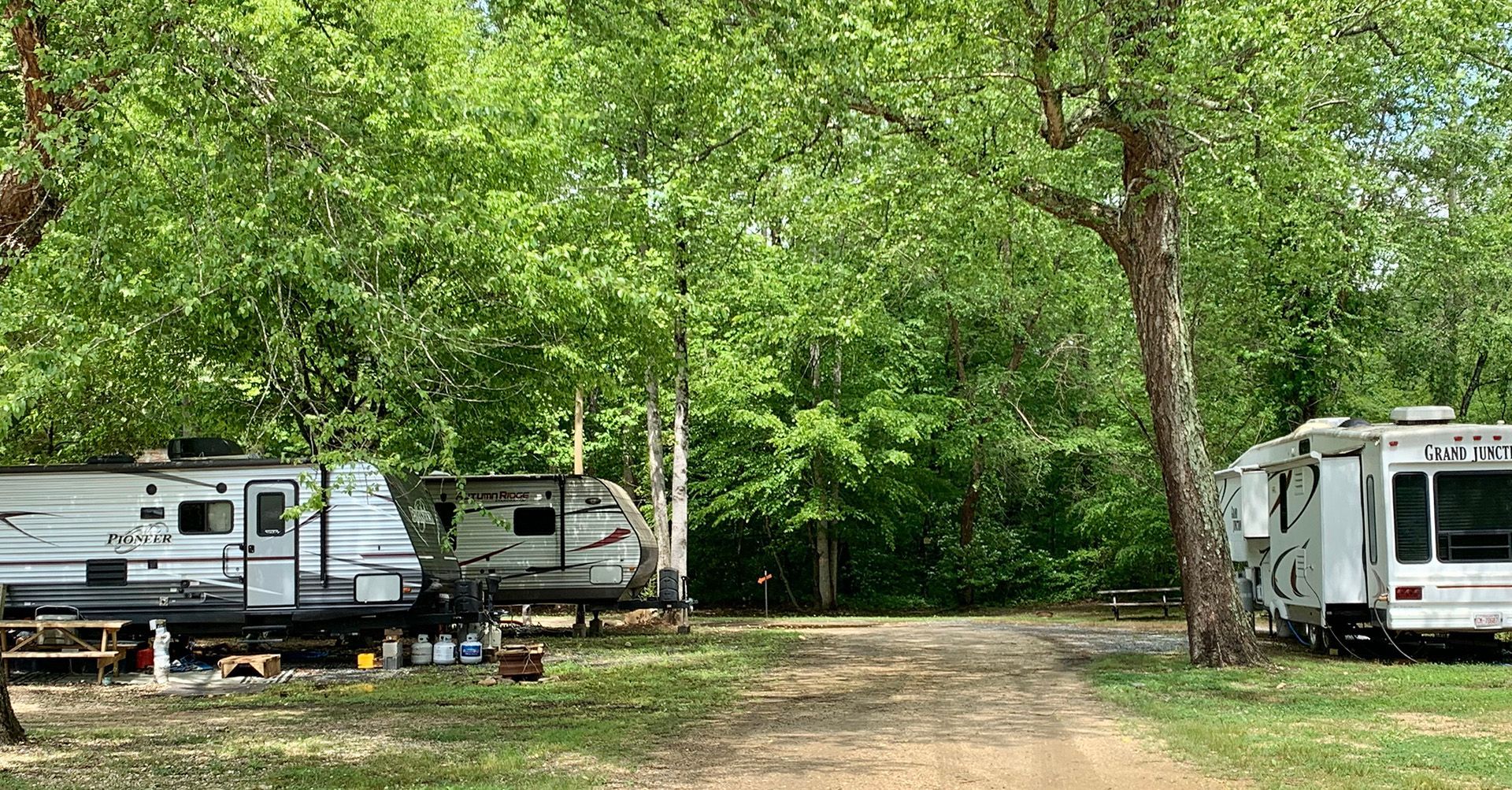 A row of rvs parked in a grassy area surrounded by trees.