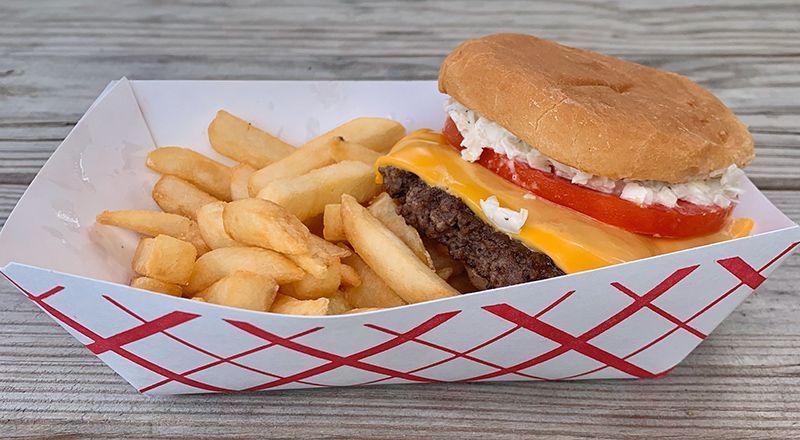 A hamburger and french fries in a paper container on a wooden table.