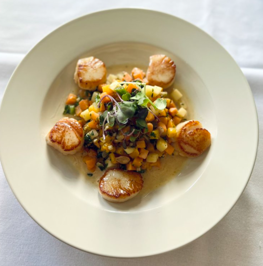 A white plate topped with scallops and corn on the cob