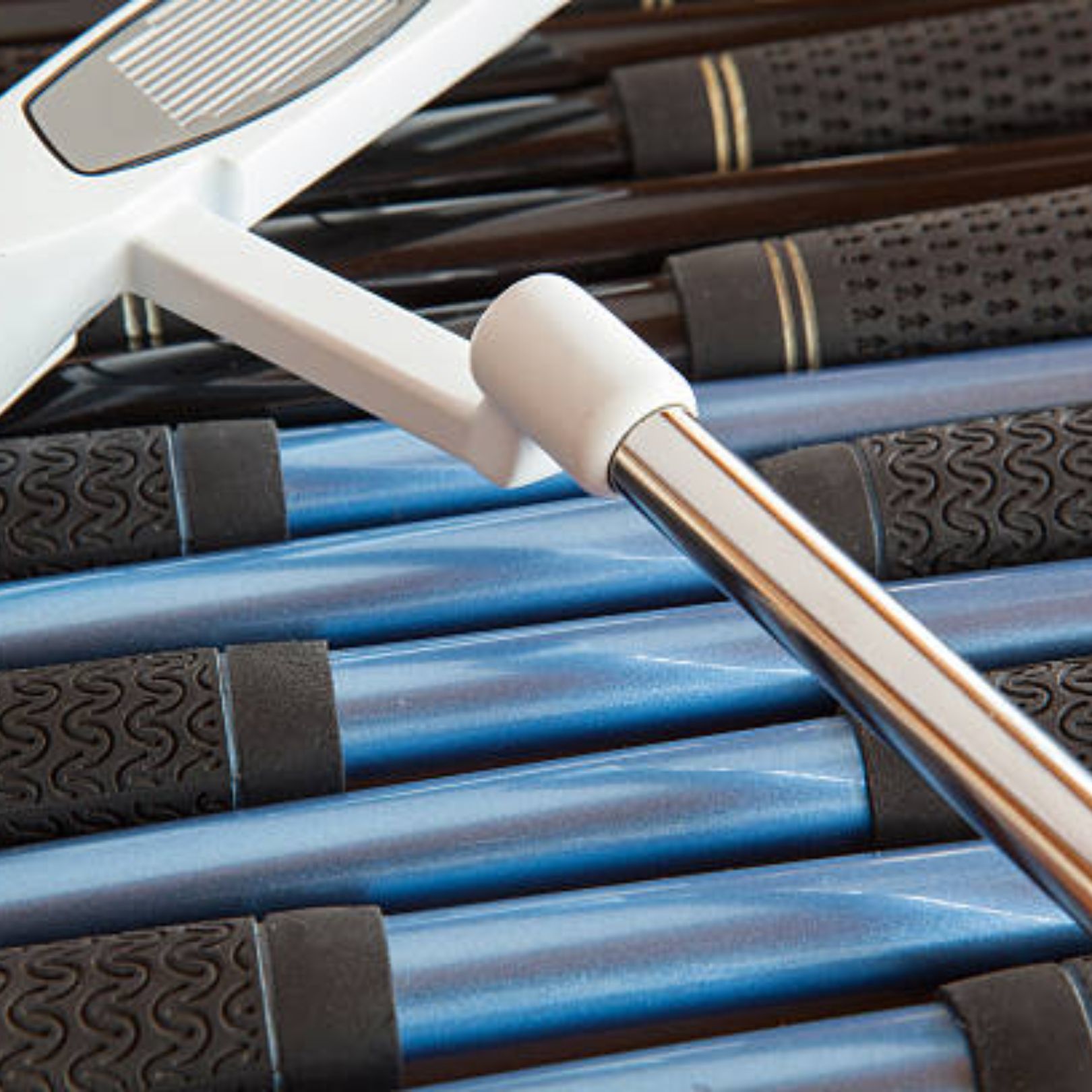 A white golf putter head sits atop a collection of blue and black golf clubs.