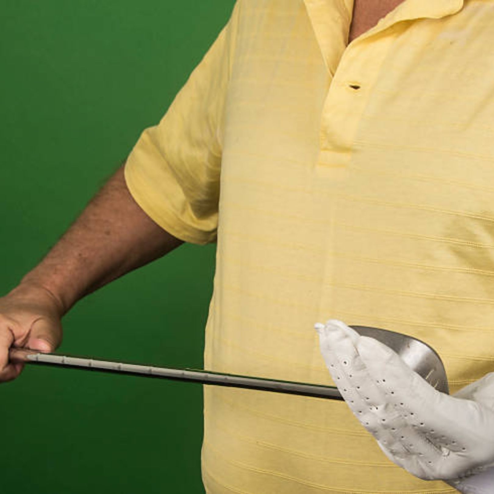A person in a yellow polo shirt wears a white golf glove and holds a golf club against a green background.