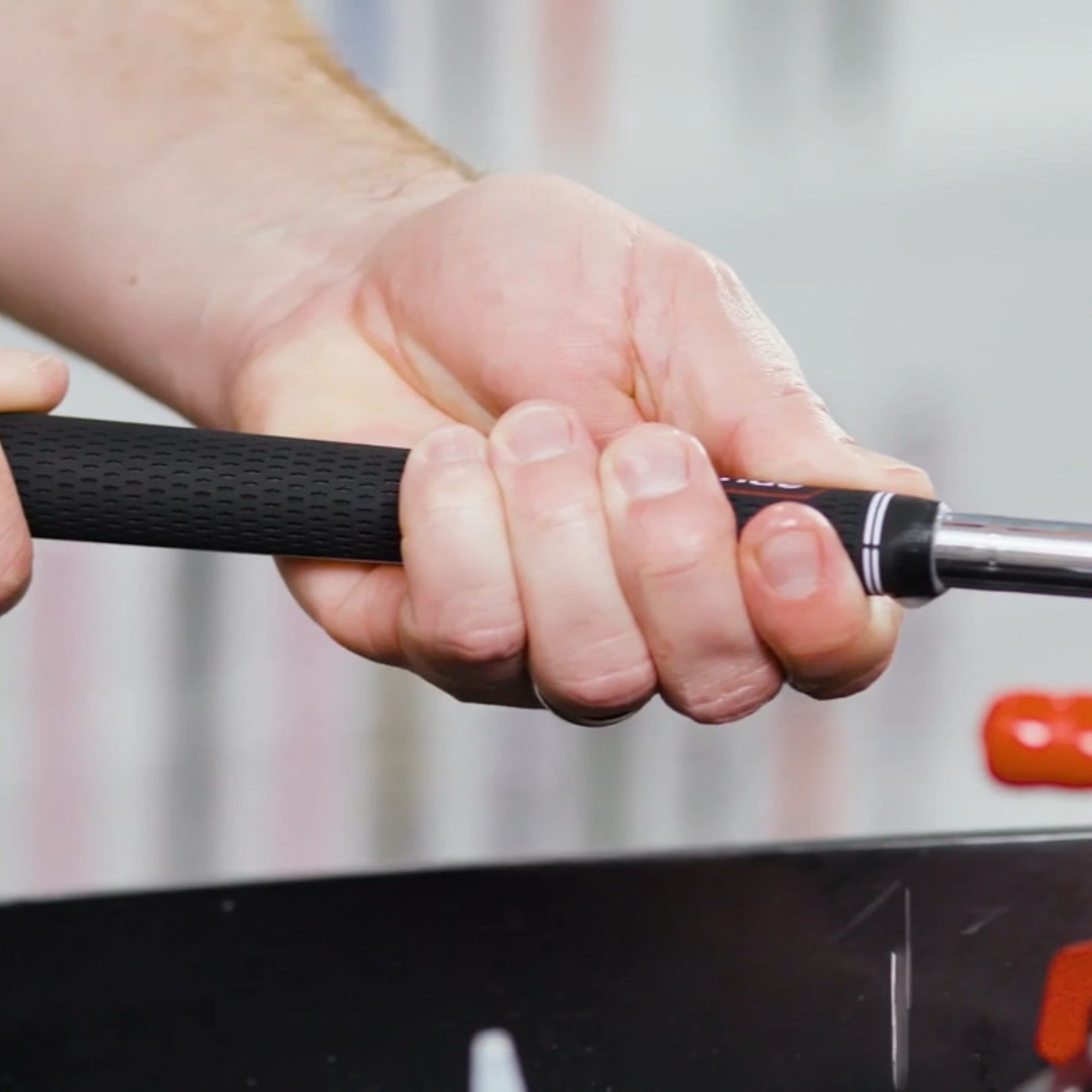 A hand grips the black, textured handle of a foosball rod above a playing surface.