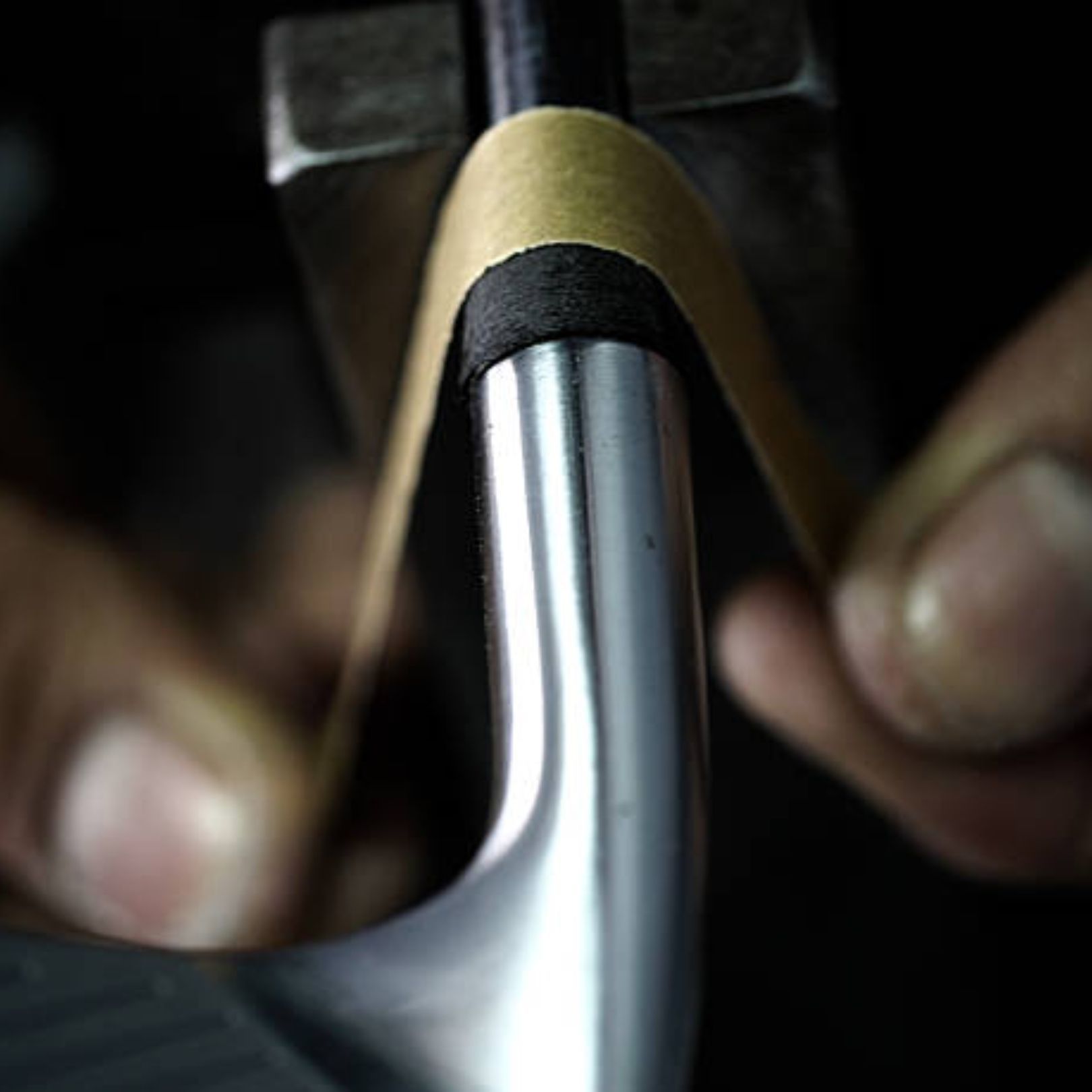 Hands wrapping a layer of tape around a golf club shaft near the clubhead.