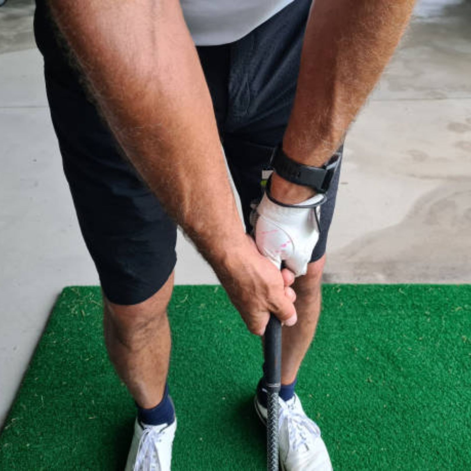 A golfer wearing a white glove holds a golf club with a neutral grip, standing on a green practice mat.