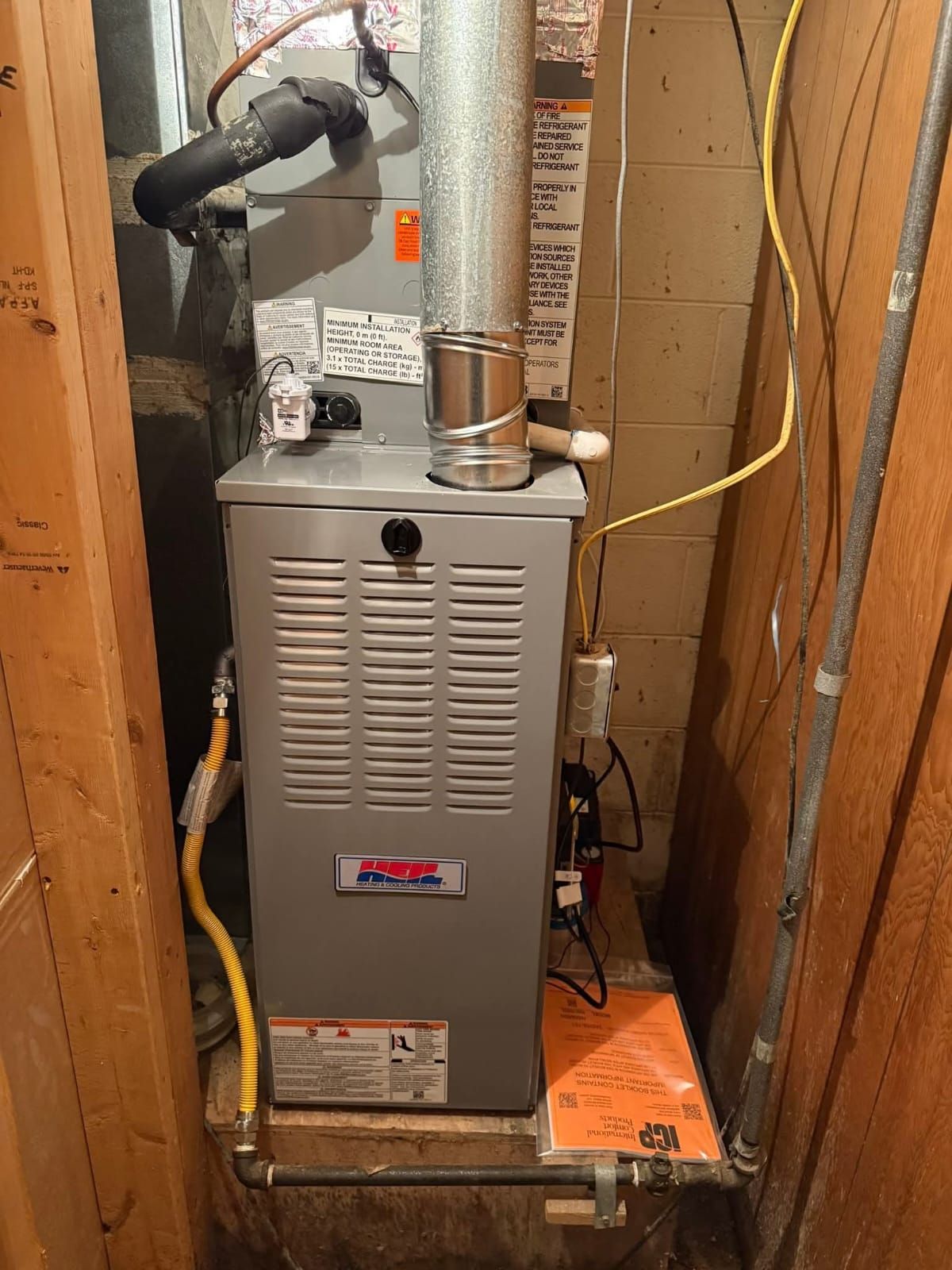 Furnace unit in a wooden enclosure with vent pipes and gas lines.