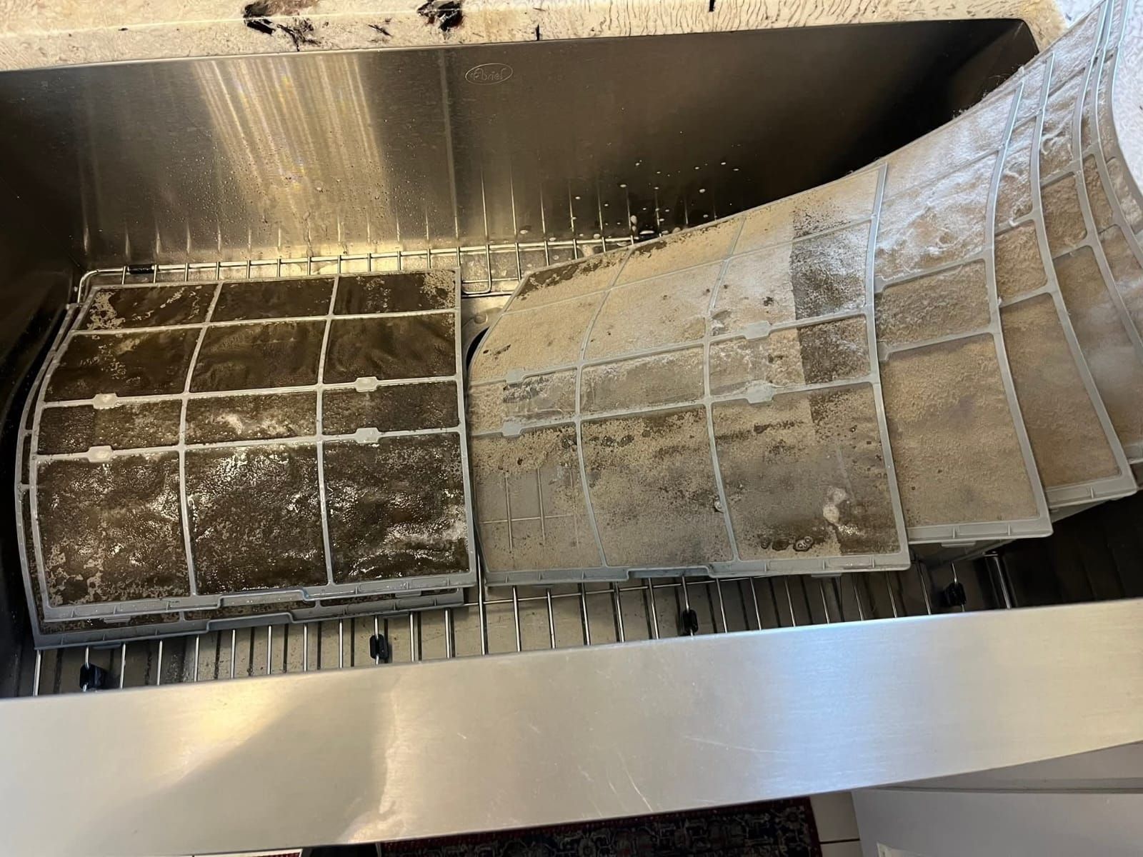 Dirty air filters soaking in a stainless steel sink.