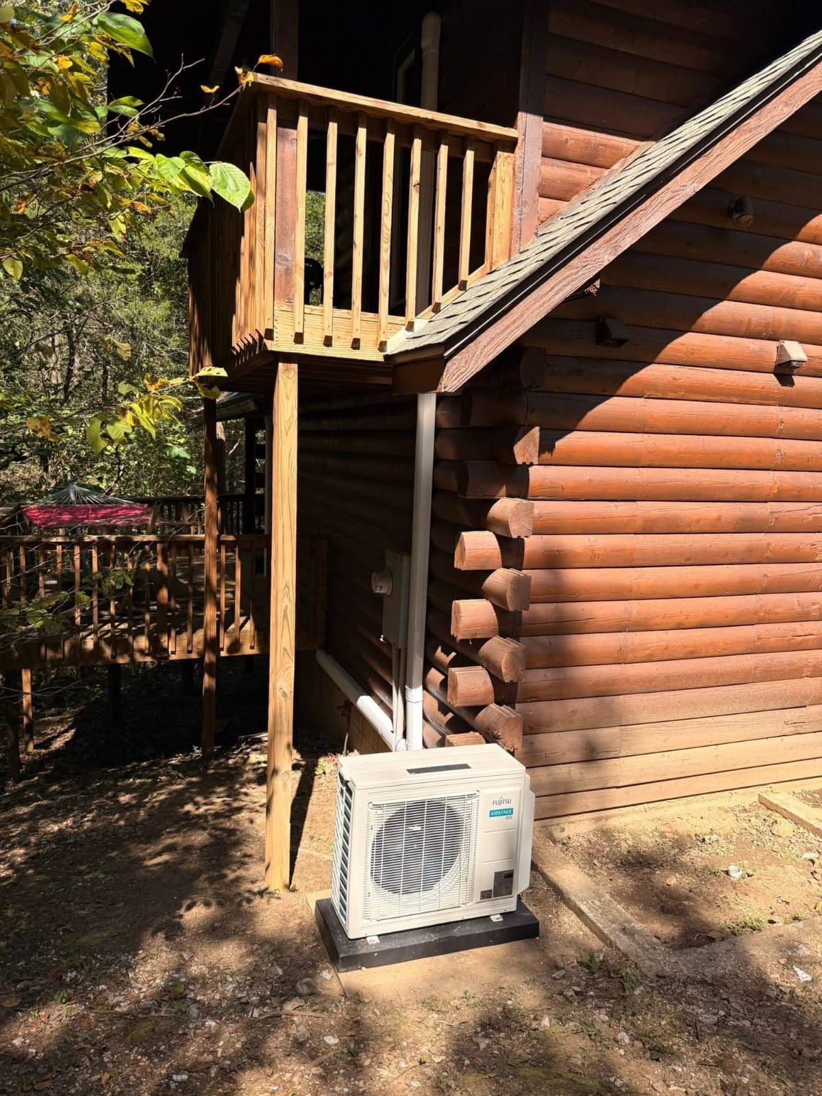 Air conditioning unit beneath a wooden deck of a log cabin style building.