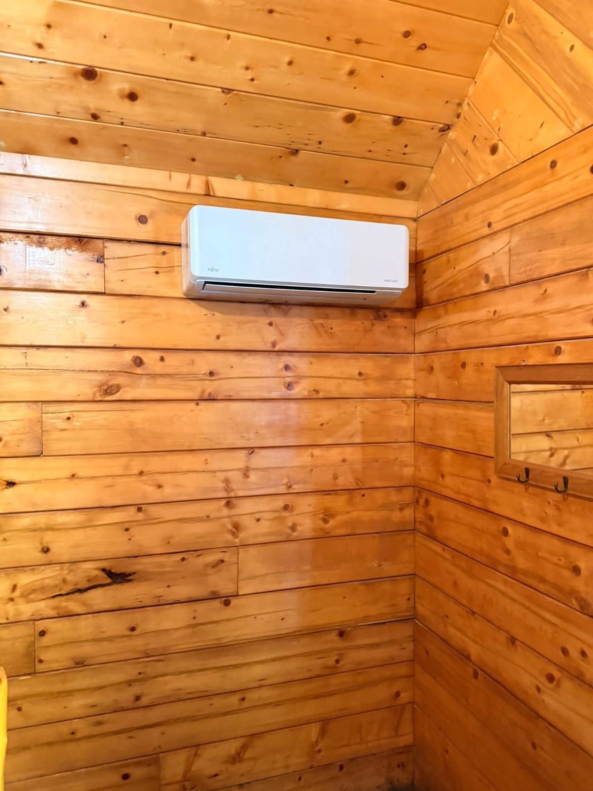 White air conditioner mounted on a wood-paneled wall inside a room.