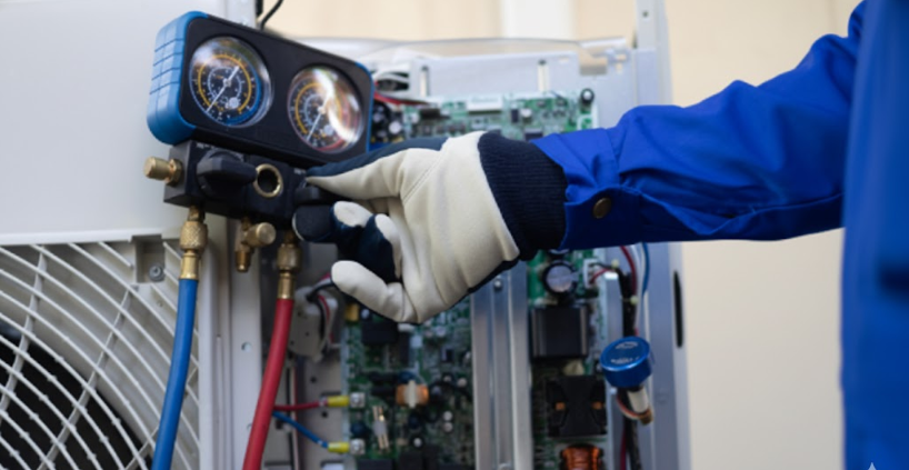 Technician in blue uniform and gloves uses gauges to service an air conditioning unit.