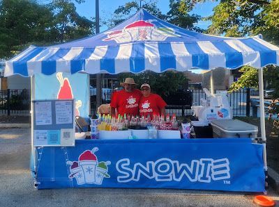 Two people are standing in front of a snowie stand.