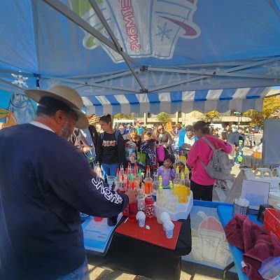 A man in a cowboy hat is standing in front of a table filled with drinks.