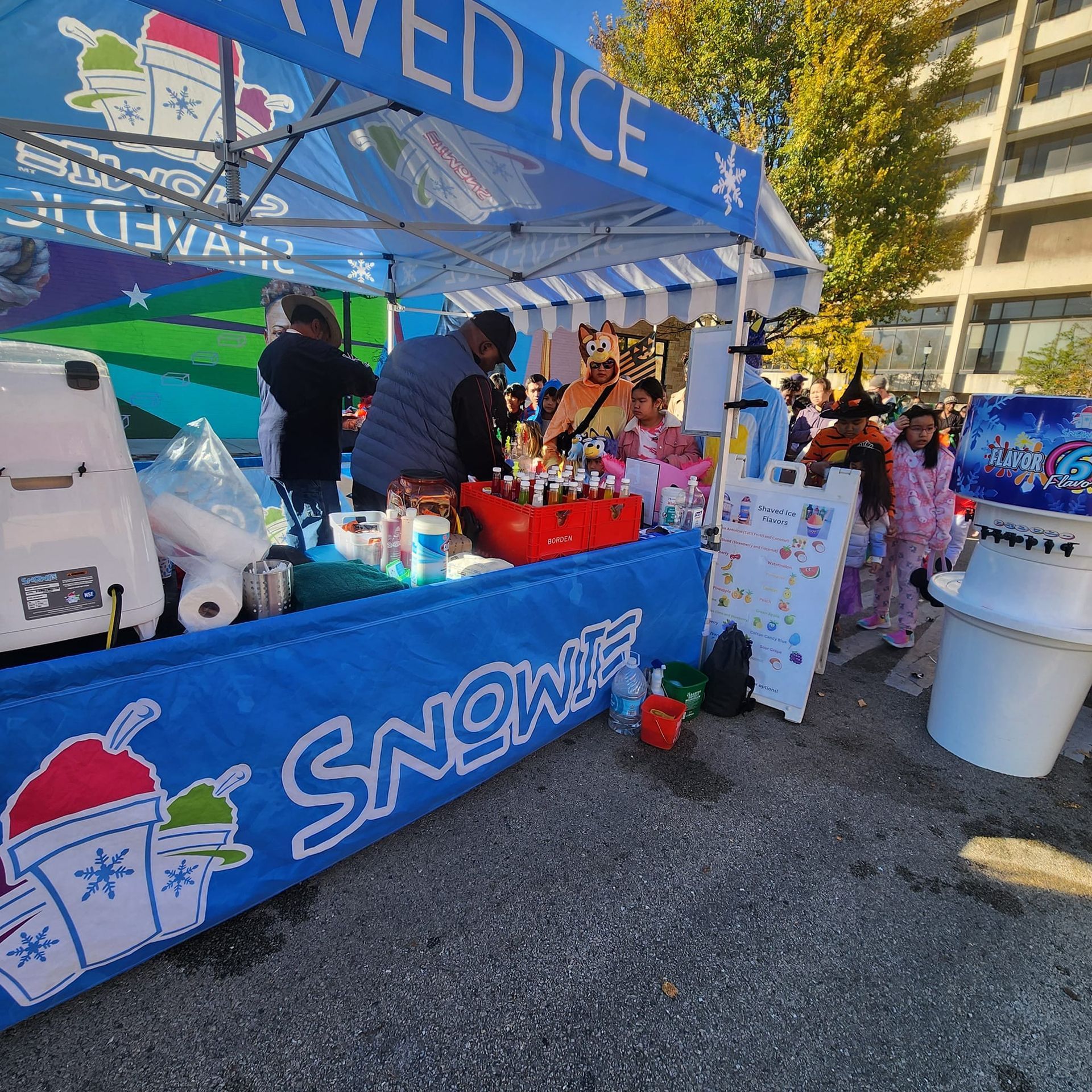 A group of people are standing around a snow ice stand.