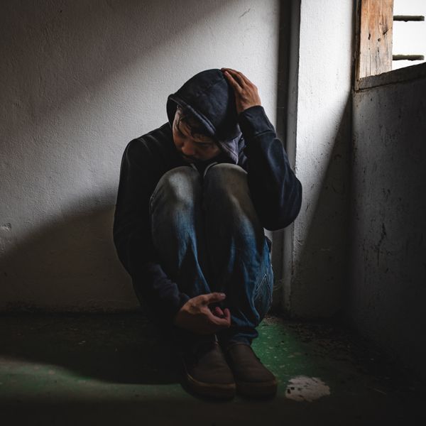 A man with an addition problem in a hoodie is kneeling down in a dark room.