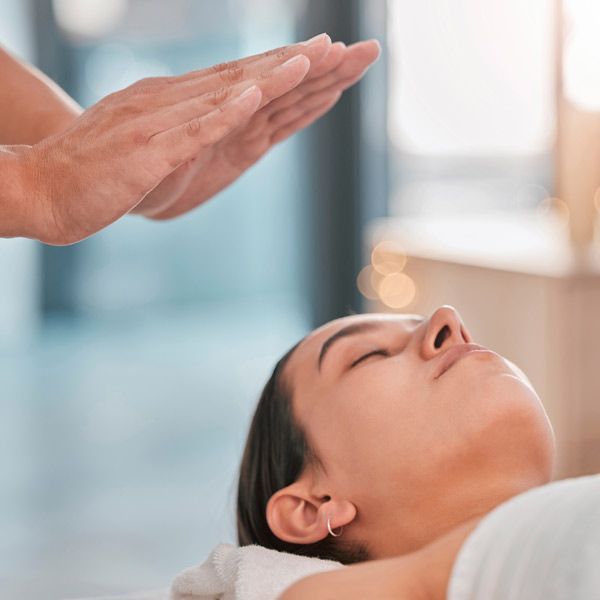 A woman is getting an Aura Cleansing Treatment with her eyes closed.