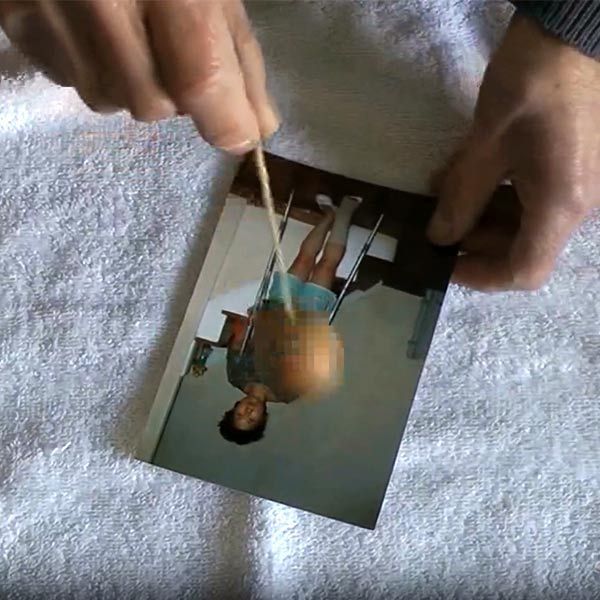 Samuel Minond is holding a picture of a woman upside down on a towel doing long-distance healing with a pendulum.