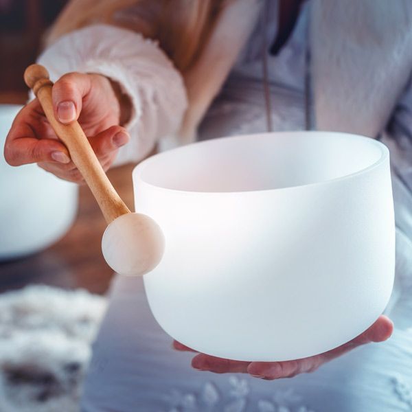 A person is holding a white bowl with a wooden stick in their hands representing sound therapy