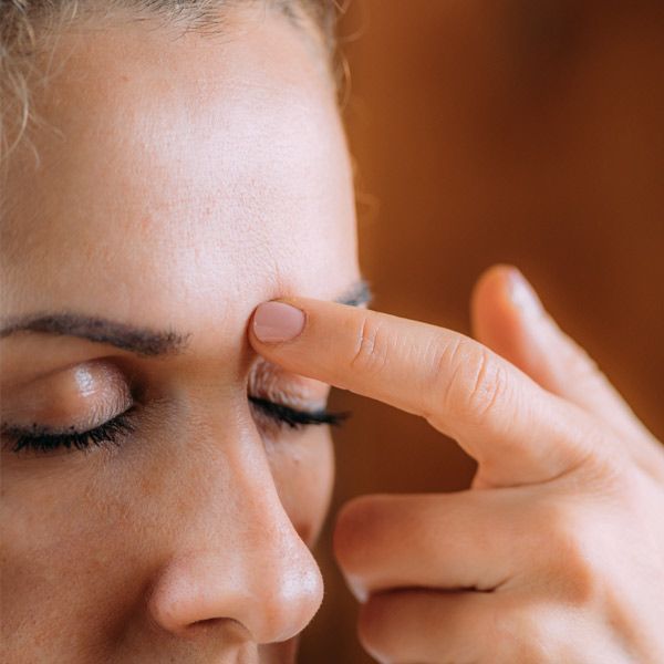 A close-up of a woman's face with her finger on her forehead representing Meridian Energy Healing