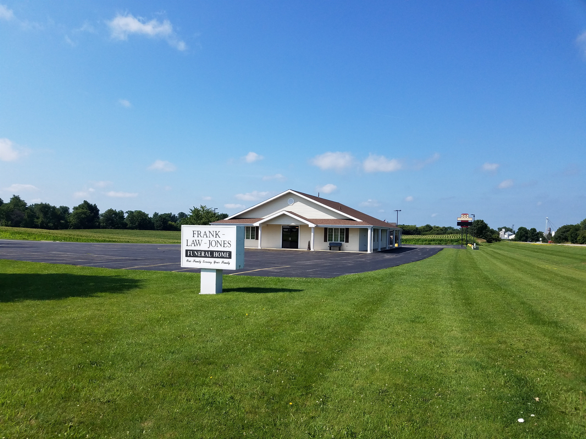 A white building with a sign in front of it is sitting on top of a lush green field.