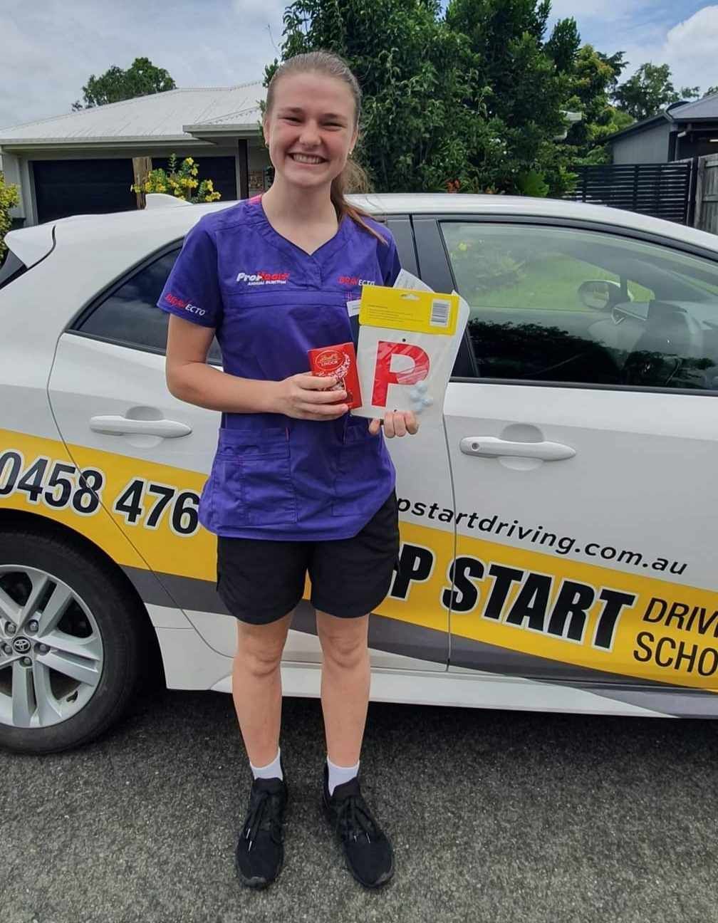 A Woman is Standing in Front of a White Car Holding a P Plate — Top Start Driving School In Cannonvale, QLD