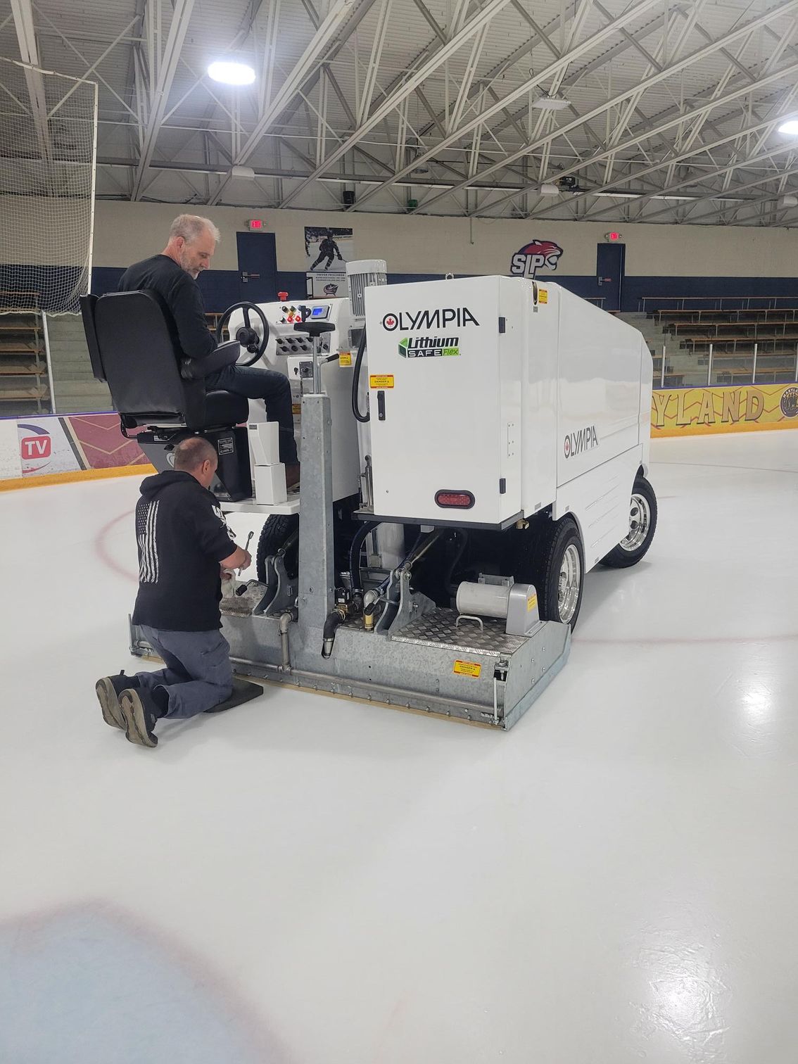 Two people working on an ice resurfacer on an ice rink.
