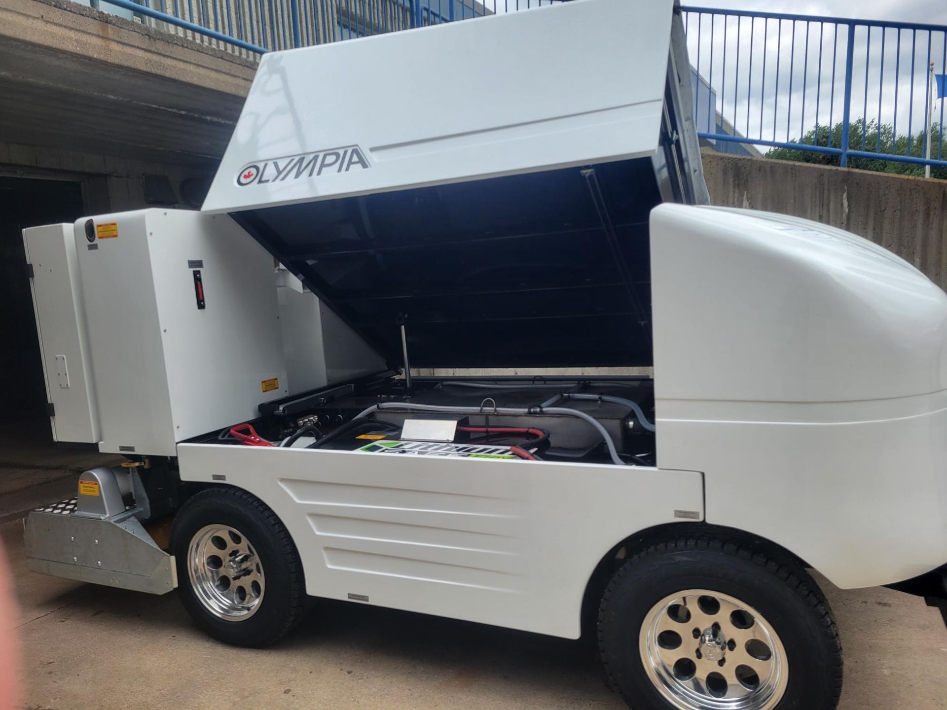 A white vehicle with the hood open is parked in a parking lot.