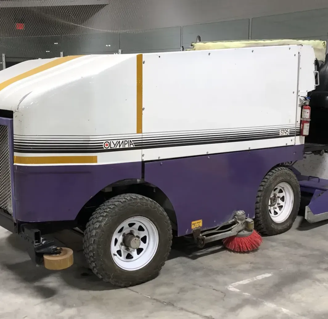 A purple and white ice hockey cleaner is parked in a parking lot.