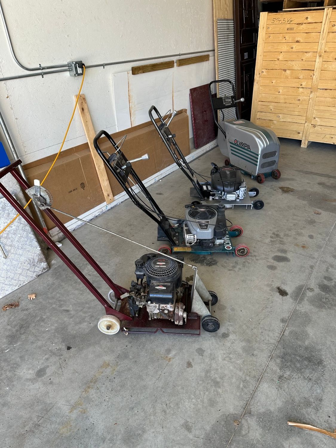Three vacuum cleaners are sitting on a concrete floor in a garage.