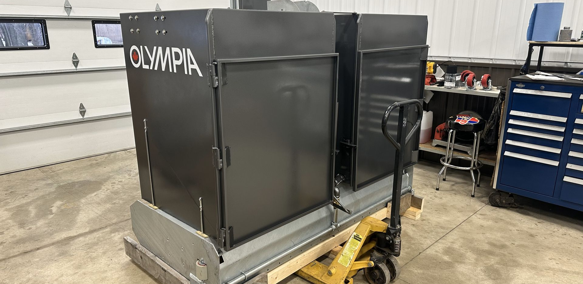 Black metal Olympia machine on a pallet jack in a workshop.