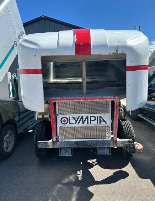 A white and red olympia trailer is parked in a parking lot.