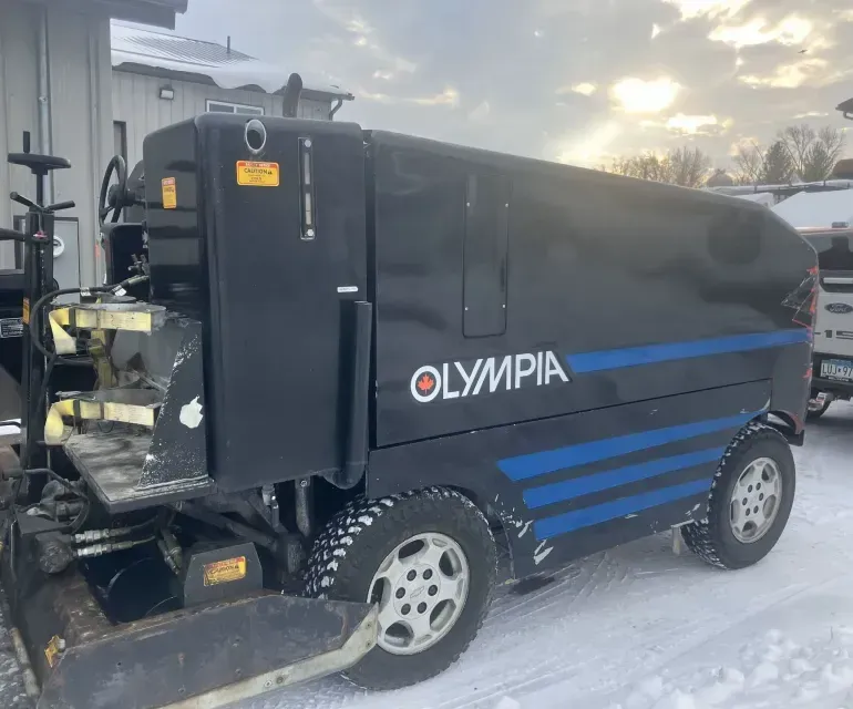 A black olympia ice hockey machine is parked in the snow.