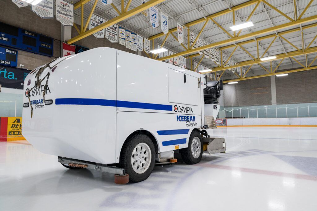 A white and blue ice truck is parked on a ice rink.