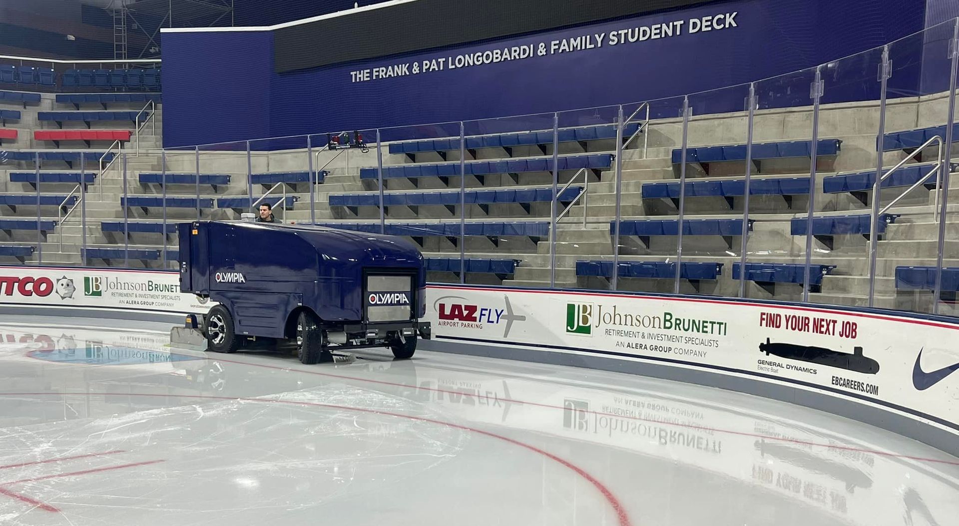 Ice resurfacing machine on hockey rink ice, arena seats in the background.