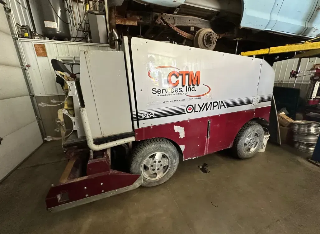 A red and white vehicle is parked in a garage under a car.