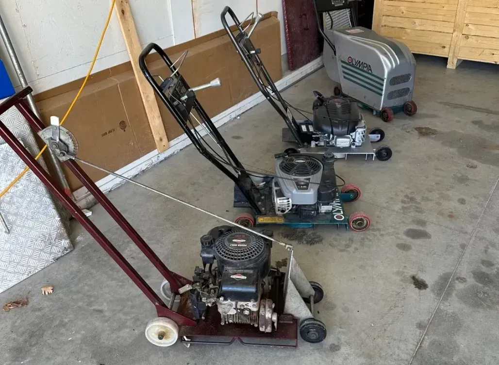 Three vacuum cleaners are sitting on a concrete floor in a garage.