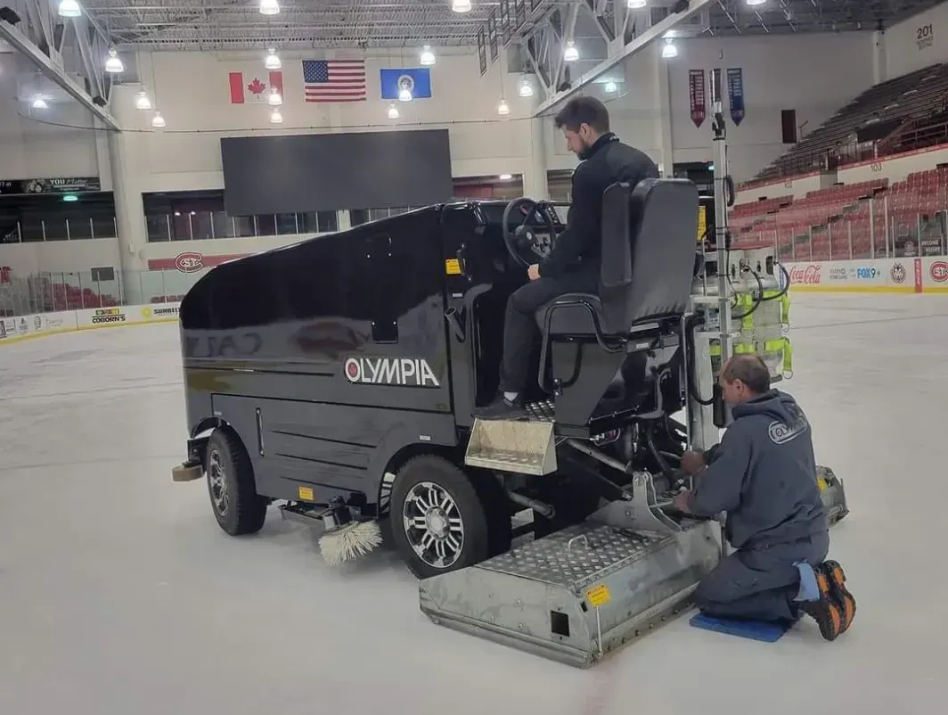 Two men are working on an ice hockey rink.