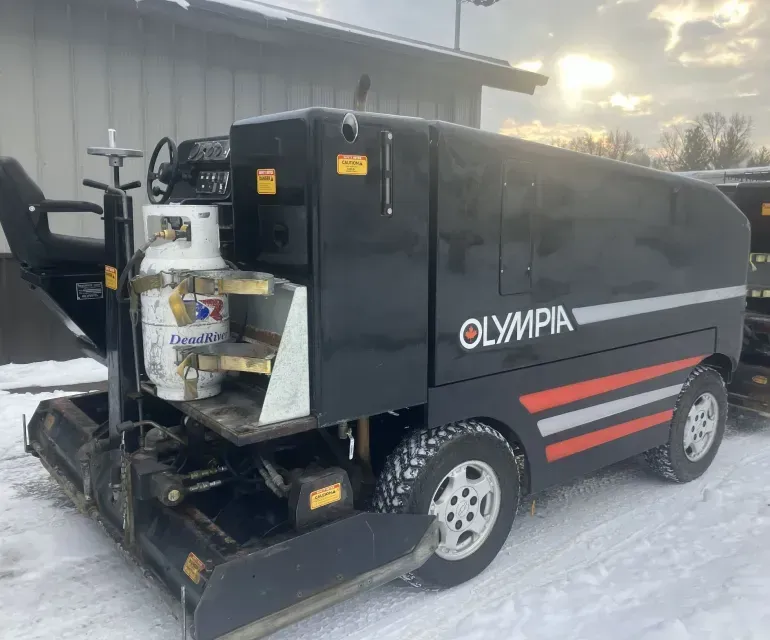 A black olympia vehicle is parked in the snow in front of a building.