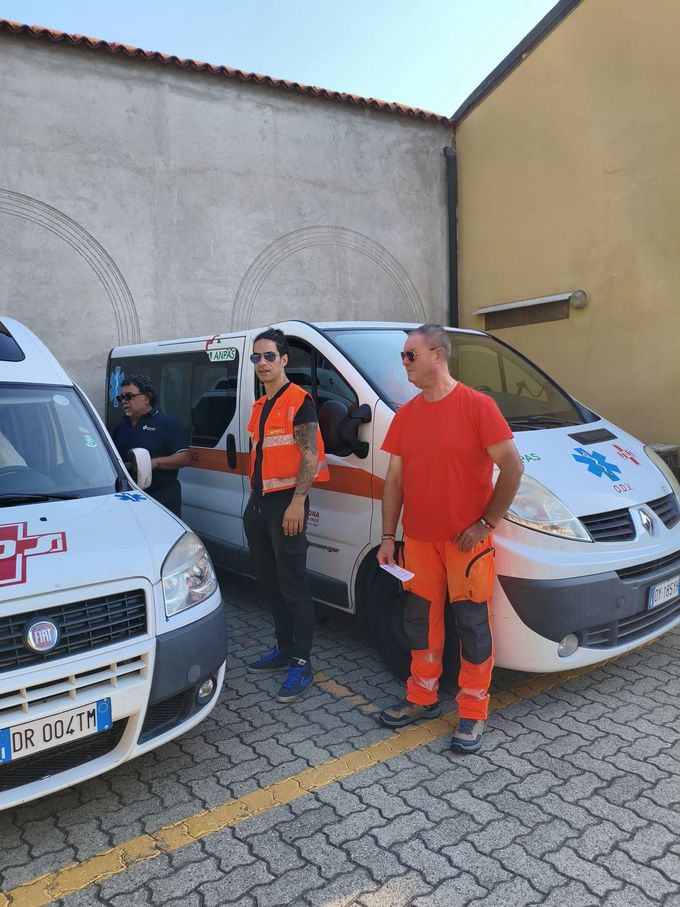 Due soccorritori della Croce Rossa con giubbotti arancioni accanto a un'ambulanza.