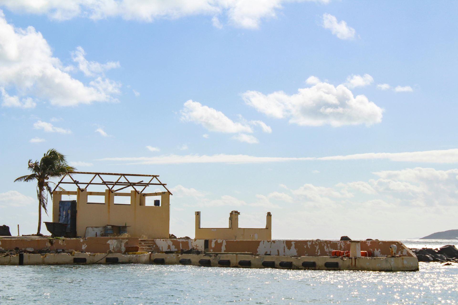 Small seaside building and stone breakwater under a bright blue sky with clouds