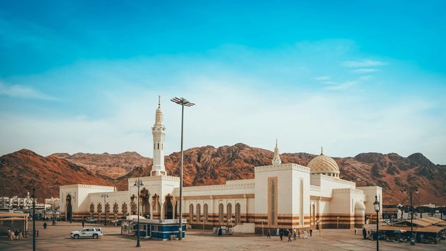 There is a mosque in the middle of a desert with mountains in the background.