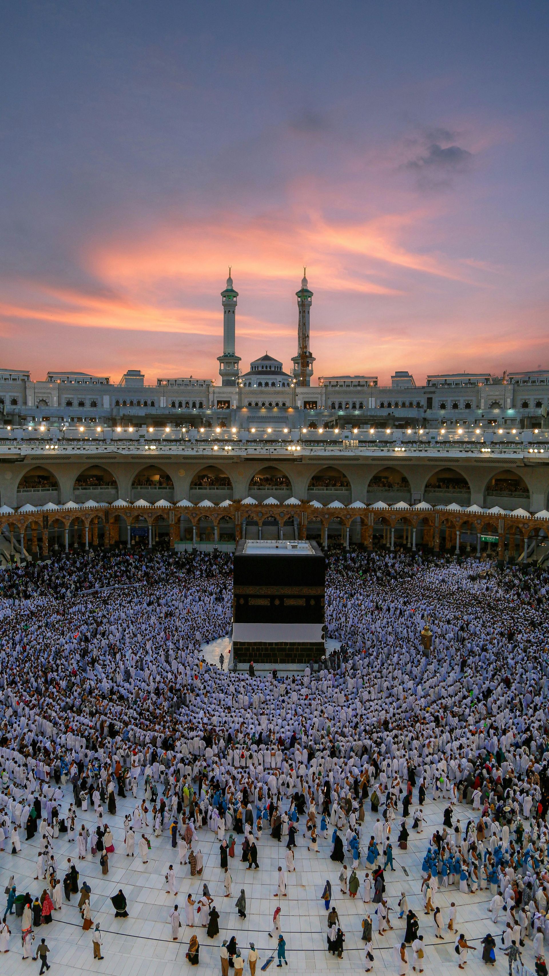 A large crowd of people are gathered in front of a mosque at sunset.