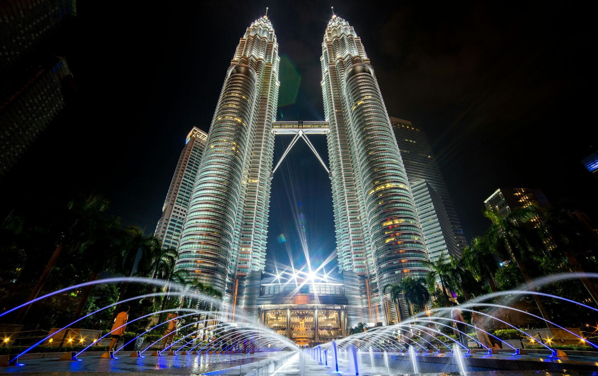 A fountain is in front of a tall building at night.
