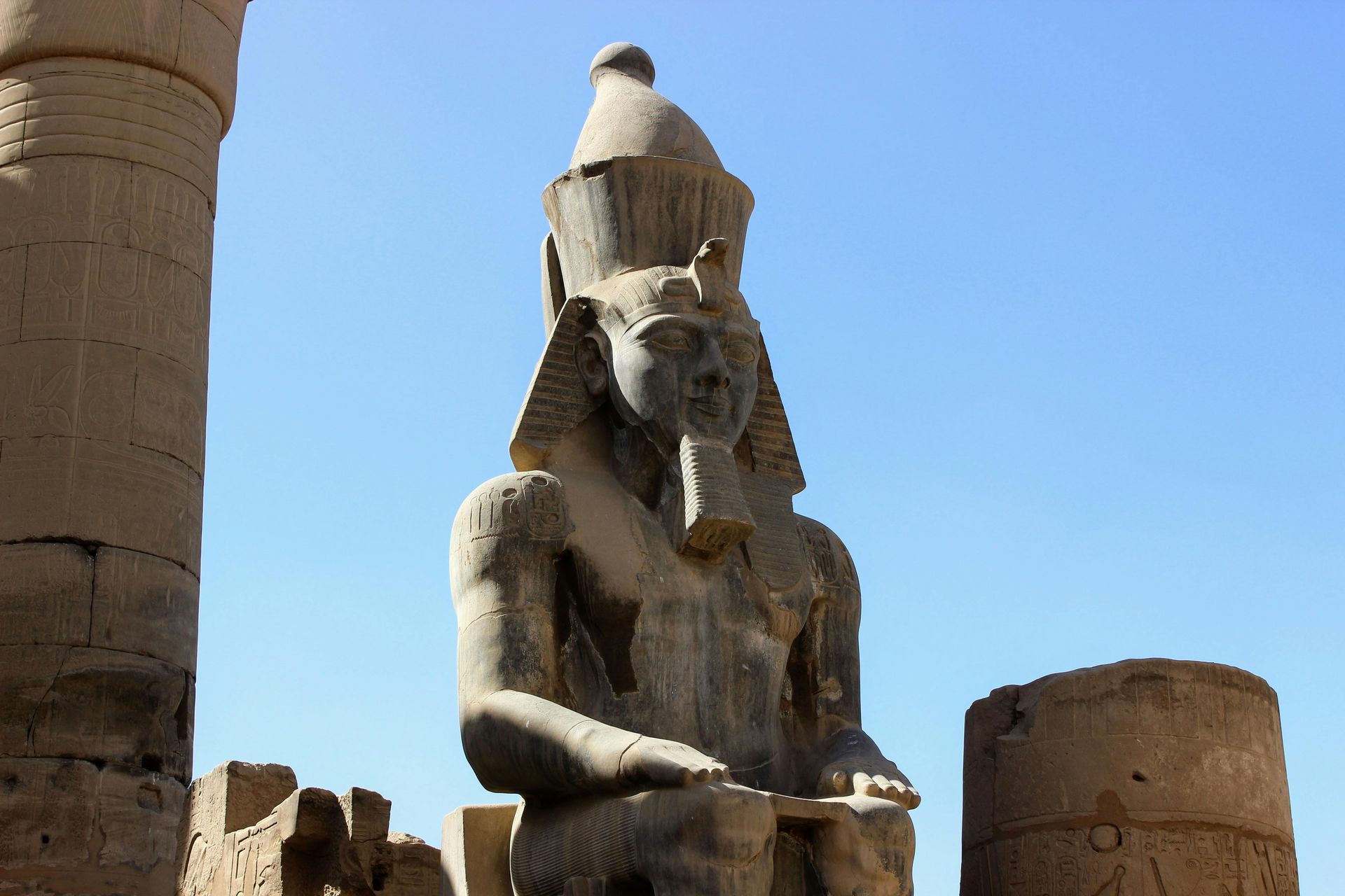 A statue of a pharaoh is sitting in front of a blue sky.